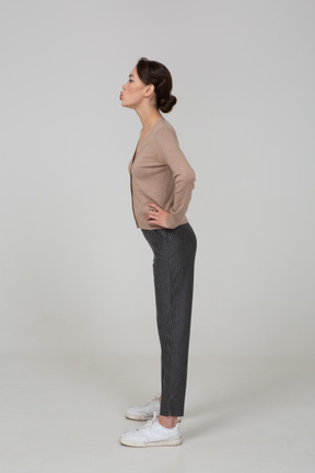 Side view of a young lady in pullover and pants pouting and putting hands on hips