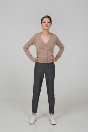 Front view of a displeased young lady in pullover and pants putting hands on hips
