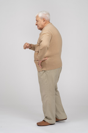 Side view of an old man in casual clothes standing with hand on hip and explaining something