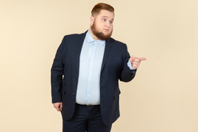 Severe looking young overweight man in suit pointing up