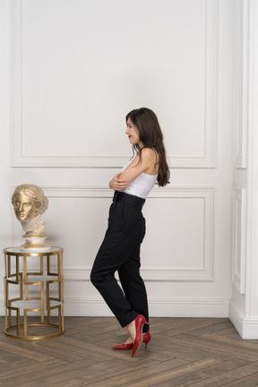 Side view of a grimacing young female crossing hands while standing near golden greek sculpture