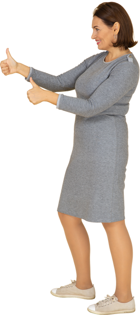 Vista lateral de uma mulher de vestido cinza mostrando os polegares para cima