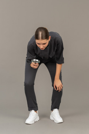 Front view of a young woman in a jumpsuit holding a magnifying glass