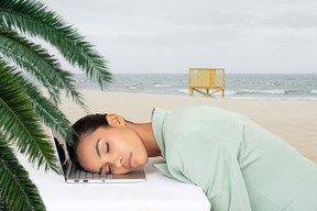 Woman sleeping on laptop on the beach