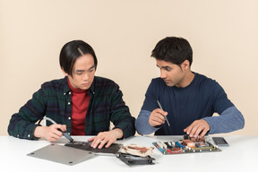 Dois geeks sentados à mesa e consertando alguns detalhes