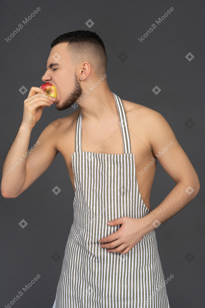 Young man wearing apron is biting an apple