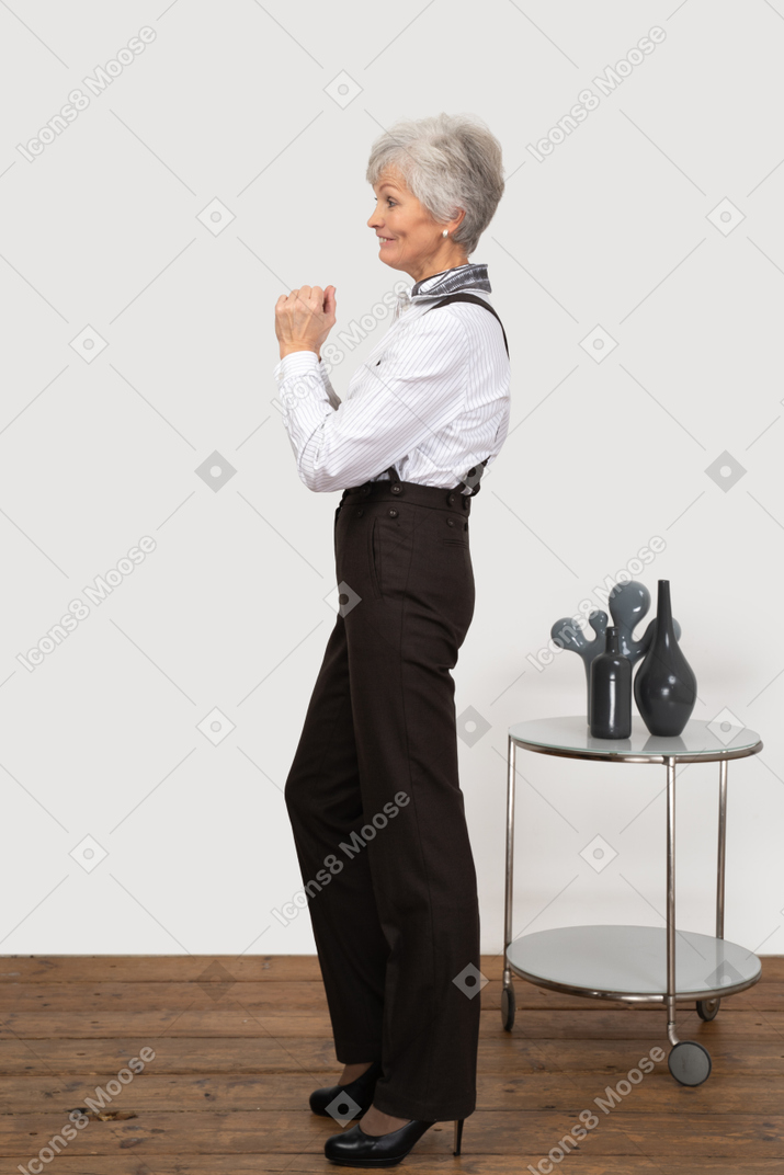 Side view of a smiling old lady in office clothing holding hands together