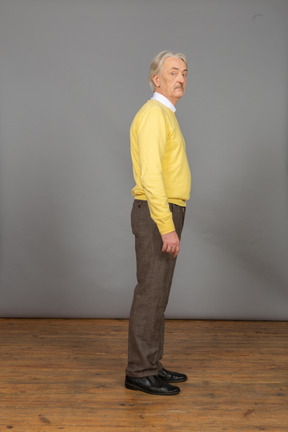 Вид сбоку на пожилого любопытного человека в желтом пуловере, поворачивающего голову и смотрящего в камеру