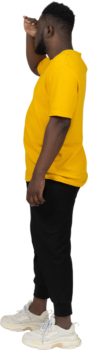 Side view of a young dark-skinned man in yellow t-shirt looking for something
