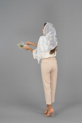 手にノートとカメラに戻って立っている若いイスラム教徒の女性