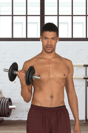 A shirtless man holding a dumbbell in a gym