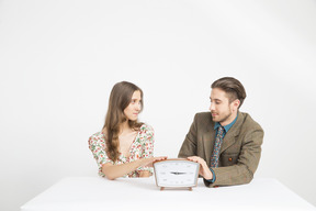 Casal sentado à mesa e segurando um relógio