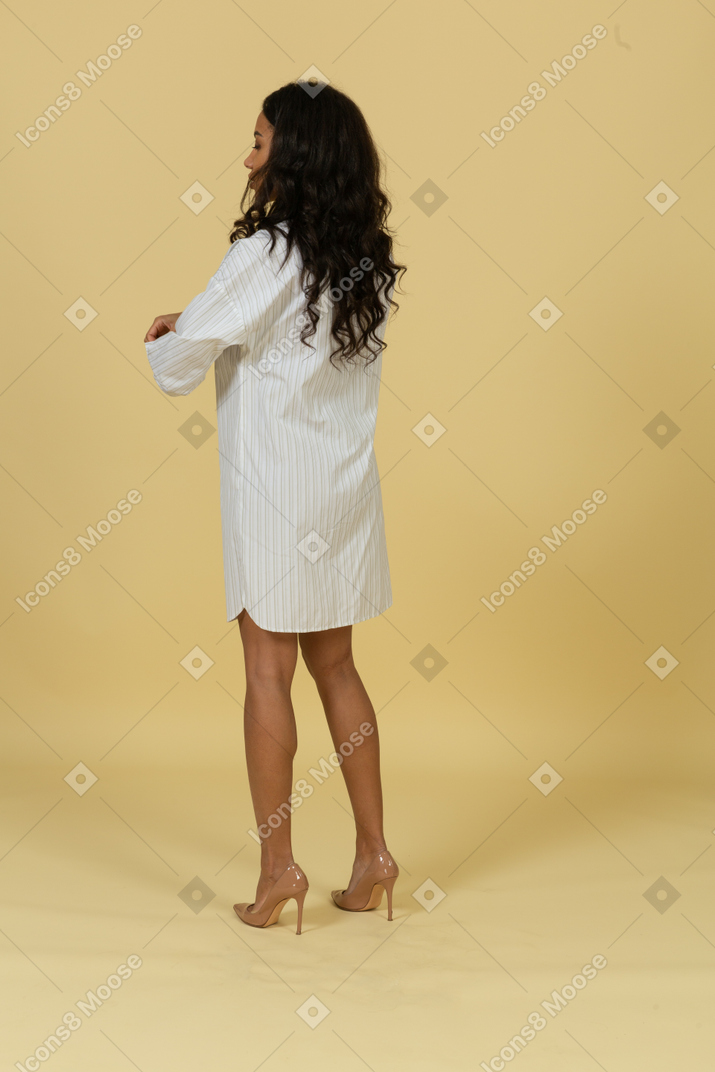 四分之三的后视图，穿着白色连衣裙的黑皮肤的年轻女性，卷起袖子