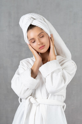 Mulher de roupão massageando o rosto com os olhos fechados