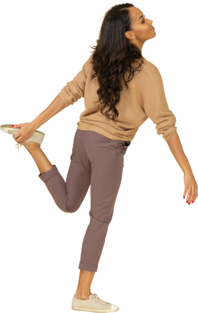 Vista posterior de tres cuartos de una mujer joven de piel oscura tocándose el tobillo