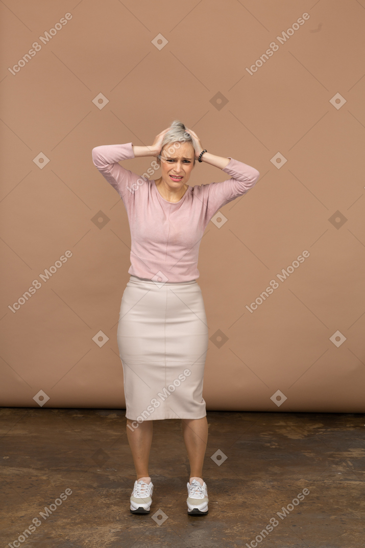 Вид спереди эмоциональной женщины в повседневной одежде, стоящей с руками на голове