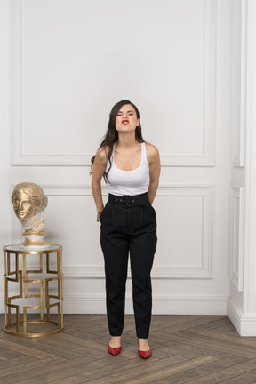 Front view of a grimacing young female holding hands behind while standing near golden greek sculpture