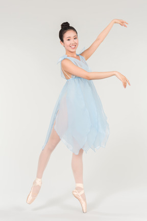 Молодая азиатская балерина в прозрачном голубом платье стоит в классической балетной позе