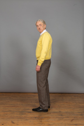 Seitenansicht eines alten überraschten mannes im gelben pullover, der kamera und grimasse betrachtet