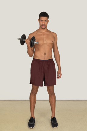 A frontal view of the handsome athletic man dressed in red shorts and black sneakers doing exercises and looking to the camera