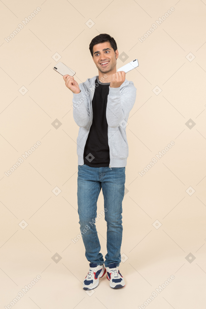 Ridere giovane uomo caucasico in possesso di due smartphone