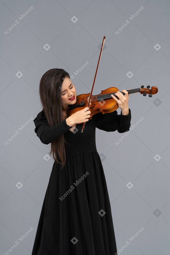Крупный план молодой эмоциональной дамы в черном платье, играющей на скрипке