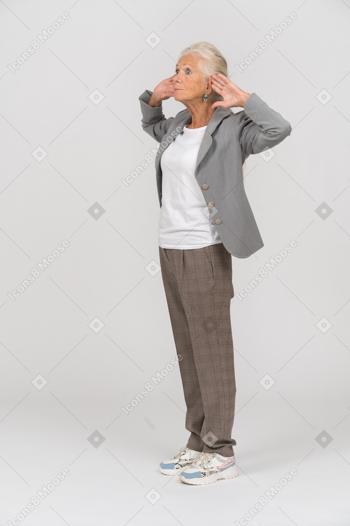 Vista lateral de uma senhora idosa de terno posando com as mãos atrás da cabeça