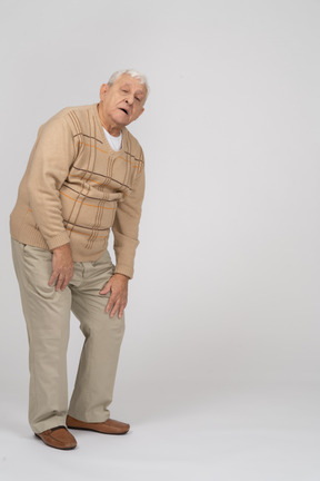 Old man in casual clothes touching knee and looking at camera