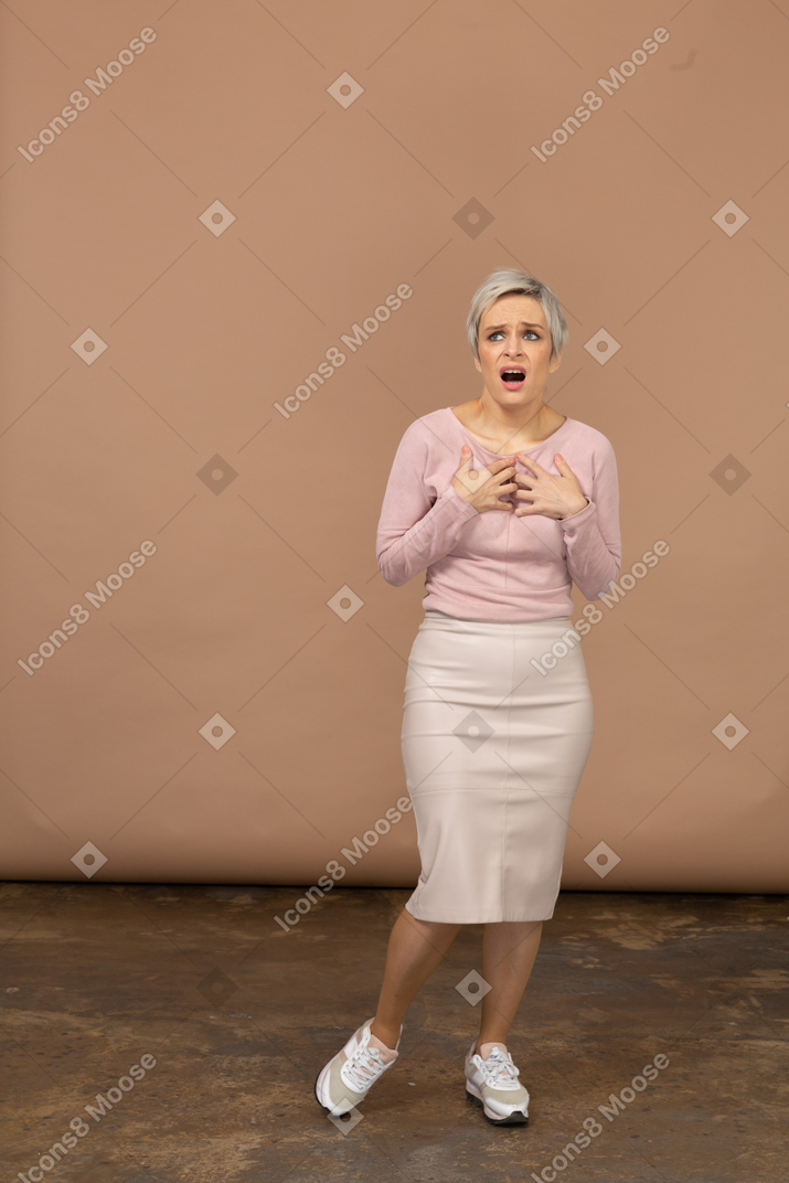 Vue de face d'une femme impressionnée dans des vêtements décontractés debout avec les mains sur la poitrine