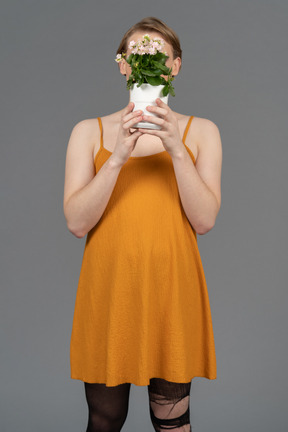 Portrait d'une personne se cachant le visage derrière un pot de fleurs