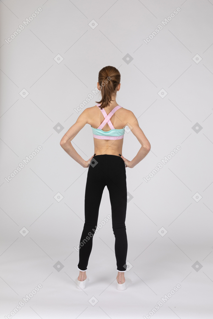 Vue arrière d'une adolescente en tenue de sport mettant les mains sur les hanches