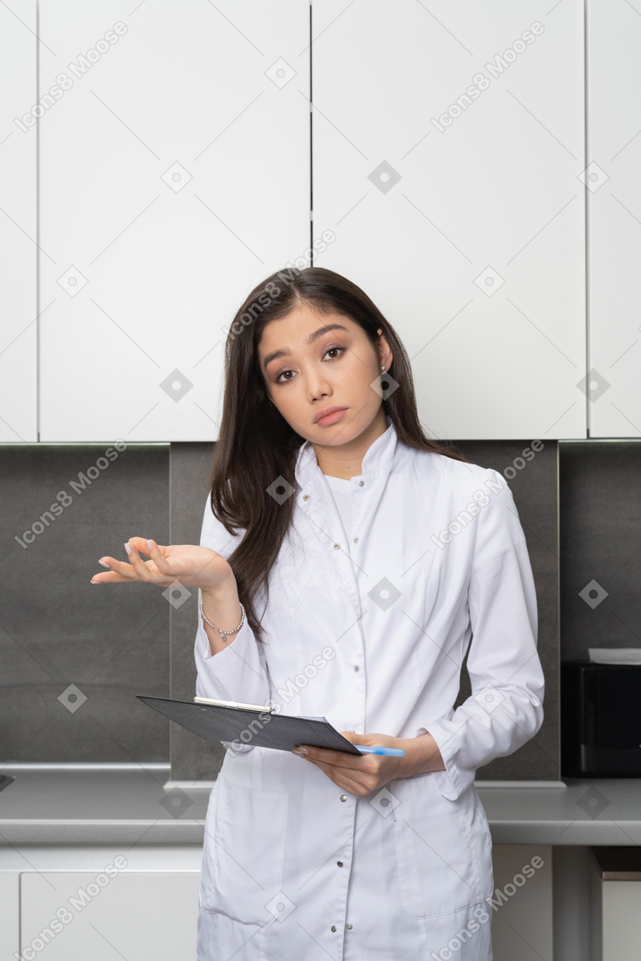Front view of a puzzled female doctor raising hand and looking at camera