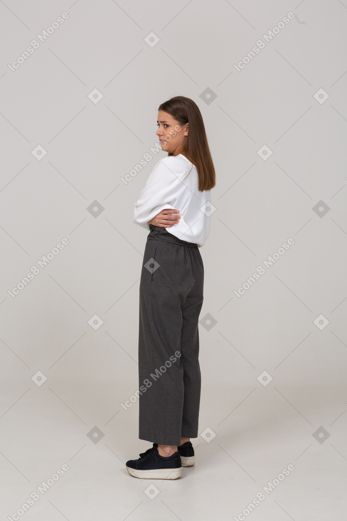 Vista posteriore di tre quarti di una giovane donna riluttante in abiti da ufficio che incrociano le braccia