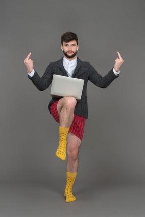 Employé de bureau avec ordinateur portable debout sur une jambe et montrant le majeur