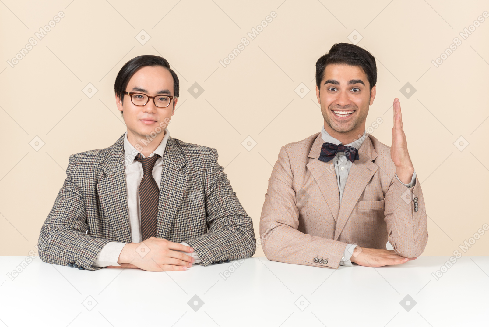 Two young nerds sitting at the table and one of them is raising hand