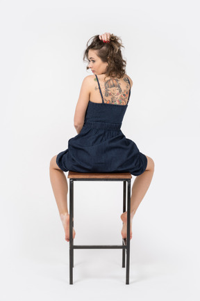 Young tattooed woman sitting on bar chair back to camera