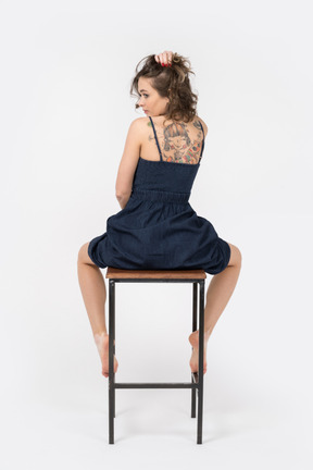 Jeune femme tatouée assise sur une chaise de bar dos à la caméra