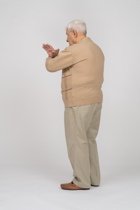 Vista lateral de un anciano con ropa informal que muestra un gesto de parada
