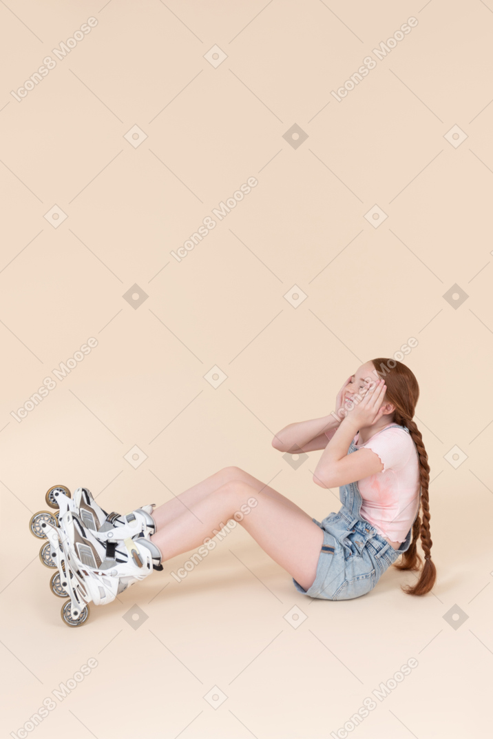 Teenage girl wearing rollerblades sitting and touching her forehead