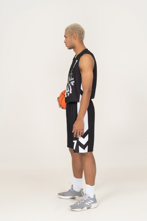 Vista laterale di un giovane giocatore di basket maschile che tiene una palla