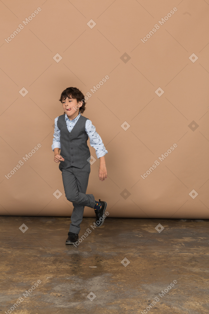 Vista frontal de um menino de terno cinza em pé com as pernas cruzadas