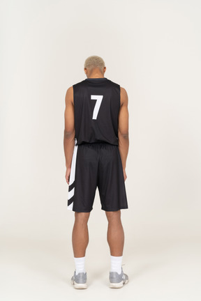 Vista posteriore di un giovane giocatore di basket maschile in piedi immobile e guardando in basso