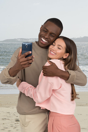 A man and a woman taking a selfie on a beach