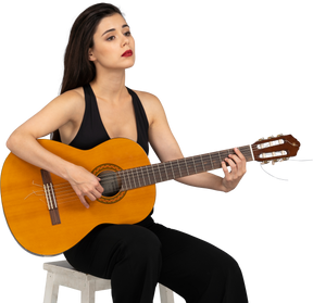 坐着的年轻女子，穿着黑色西装，拿着吉他，抬头的四分之三的视图