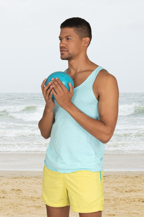 A man standing on a beach holding a blue ball