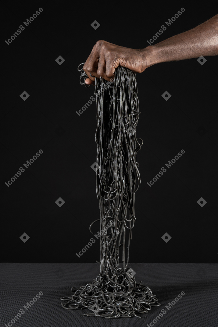 Close-up of a human hand holding black pasta with cherry tomato