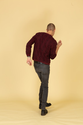 Vista traseira de um jovem dançando em uma blusa vermelha levantando a perna