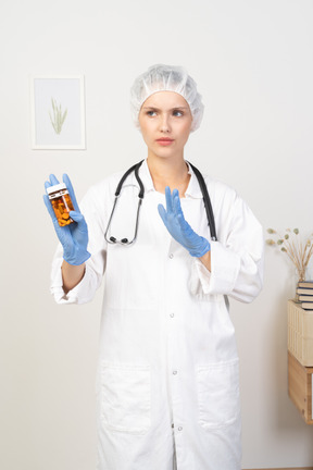 Vista frontal de una joven doctora sosteniendo un frasco de pastillas