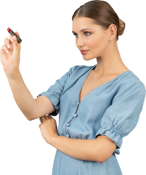 Vista di tre quarti di una giovane donna in abito blu con in mano un rossetto