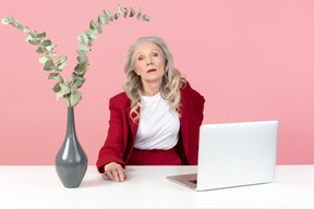 Serious looking aged woman sitting at the computer desk